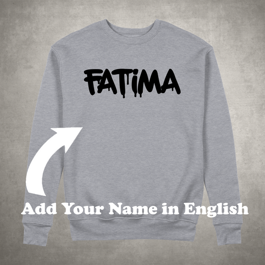 A gray sweatshirt with the name 'FATIMA' printed in black text on the front, with an arrow pointing to the text indicating a customization option that says 'Add Your Name in English'.
